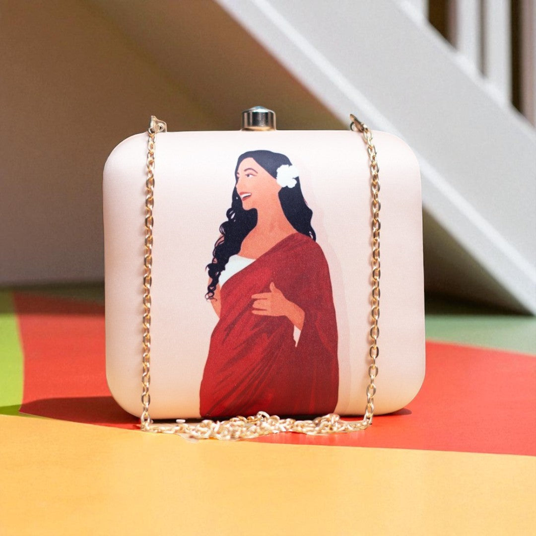 White clutch bag with a gold chain featuring an illustration of a woman in a red saree on a colorful surface.