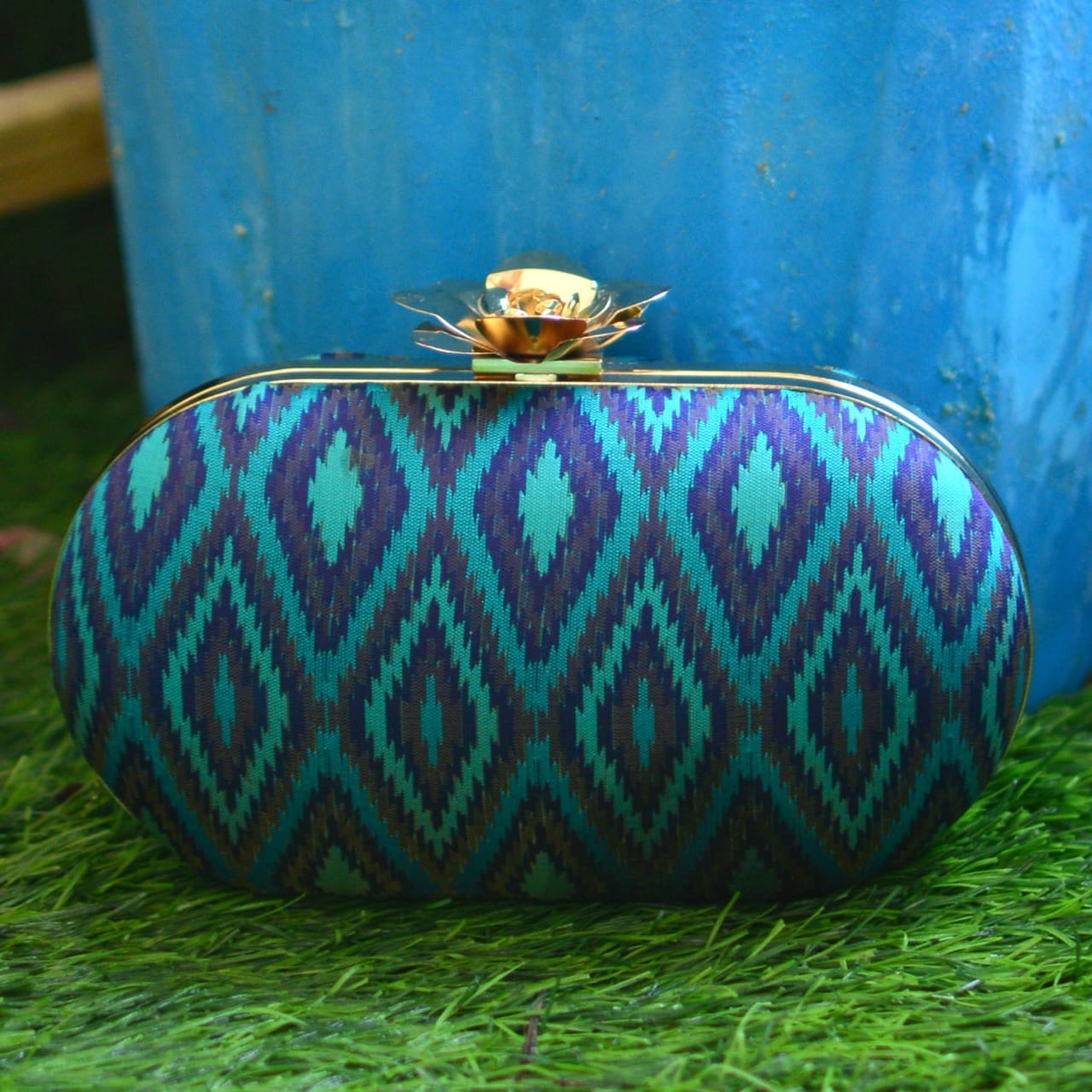 Blue and green patterned clutch bag on grass with a blue background