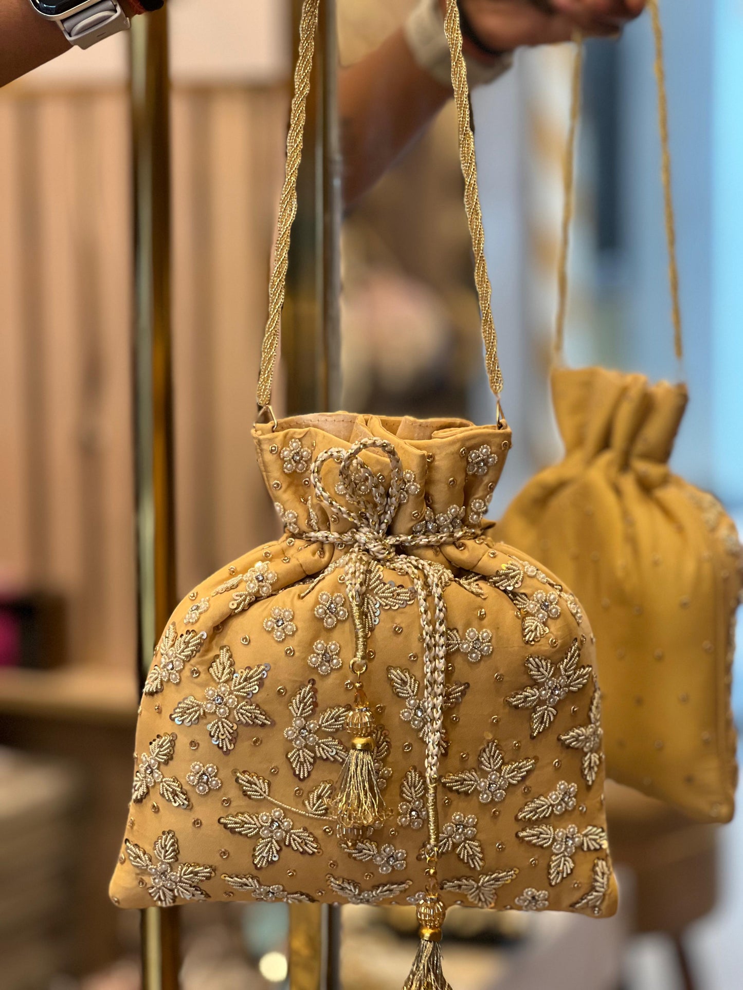 Gold embroidered handbag with a decorative tassel held by a person.