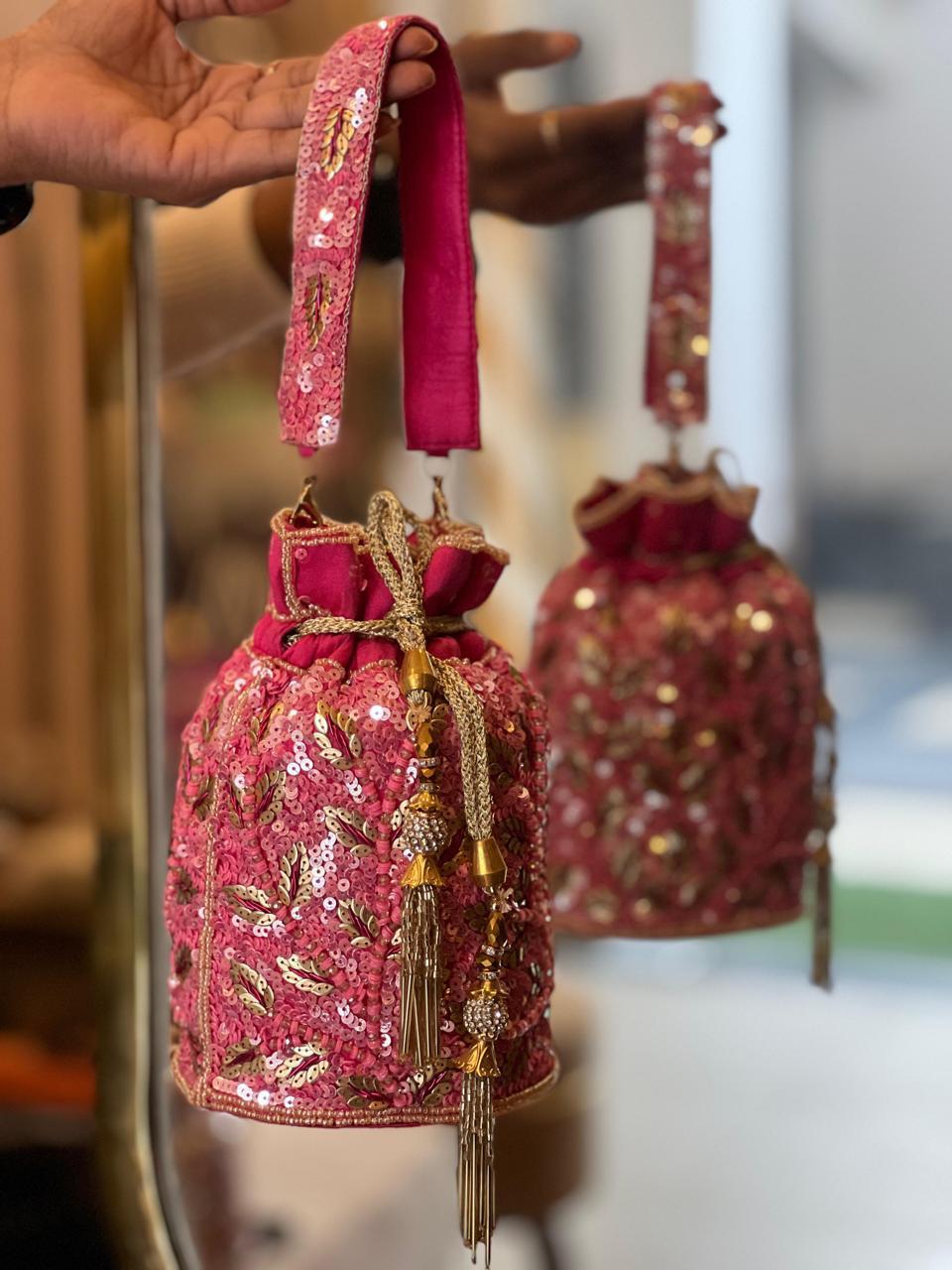 Pink embroidered handbag with gold details held by a hand against a blurred background