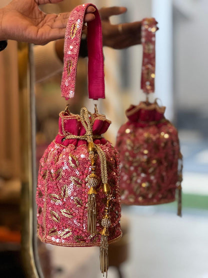 Pink embroidered handbag with gold details held by a hand against a blurred background