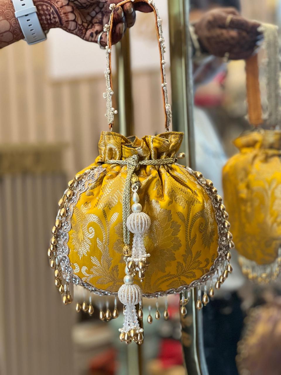 Decorative yellow bag with intricate patterns and tassels held by a hand.