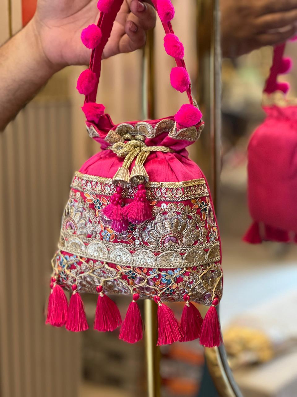 Decorative pink bag with tassels and pom-poms held by a person.